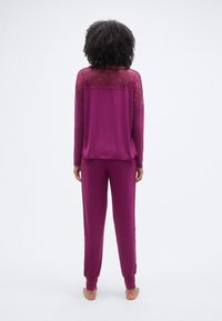 Σετ μωβ ρούχων χαλάρωσης με μακρυμάνικη μπλούζα που διαθέτει λεπτομέρεια δαντέλας στους ώμους, συνδυασμένη με παντελόνι στο ίδιο σχέδιο. Ομαλή υφή, άνετη εφαρμογή.