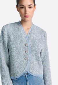 Világoskék kötött dzseki texturált mintával, fodros nyakkivágással, három ezüst gombbal és fodros szegéllyel.