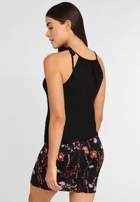 Top negro sin mangas con escote fruncido y tirantes ajustables, combinado con una falda negra ajustada con patrones florales coloridos.