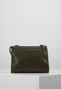 Borsa a tracolla in pelle verde oliva con una consistenza morbida, zip sulla parte superiore e manici corti. Presenta una piccola tasca esterna sul retro.