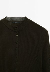 Cardigan en maille côtelée vert foncé avec un col rond et une rangée verticale de sept boutons assortis au centre.