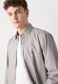 Grijze button-up shirt met een zachte textuur, voorzien van een klassieke kraag en een klein merkembleem op de borst. Draag het over een wit ondershirt.