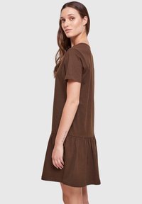 Brązowa bawełniana sukienka t-shirtowa o luźnym kroju, z krótkimi rękawami i falbaną u dołu, prezentująca gładką teksturę i prosty design.