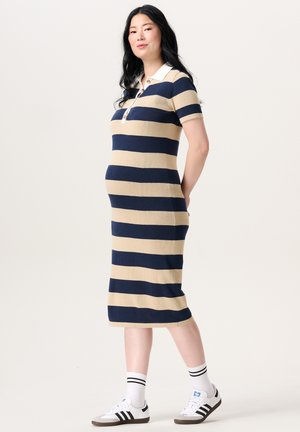Knielange gestreepte jurk in marineblauw en beige, gemaakt van zacht materiaal. Voorzien van een kraag en korte mouwen, gecombineerd met sportieve schoenen.
