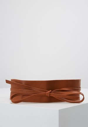 Brauner Ledergürtel mit Schleifendetail, präsentiert auf einer weißen Oberfläche vor einem einfarbigen hellgrauen Hintergrund.