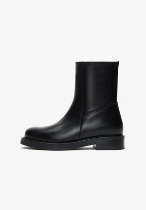 Boots chelsea en cuir noir avec un bout arrondi, texture lisse, design minimaliste et une semelle basse et robuste. Détails de couture sur le côté.