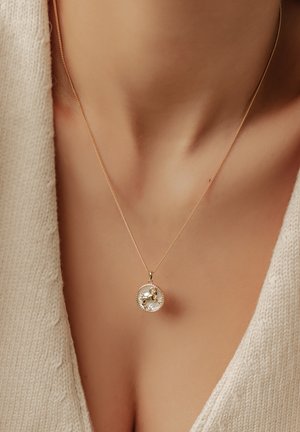 Gold necklace with a circular pendant featuring a detailed design. The pendant has a crystal-like appearance and hangs on a fine chain.