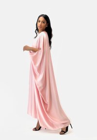 Lång, flödande kaftan i mjuk rosa satin, med vida ärmar och en avslappnad silhuett, i kombination med svarta sandaler med remmar.