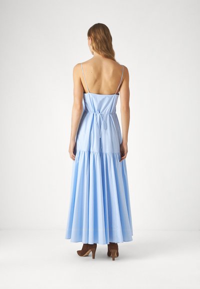 Rochie maxi fără mâneci, de culoare albastru deschis, cu un corp ajustat, funda la spate și fustă în straturi. Material neted cu o siluetă fluidă. Tocuri maro.