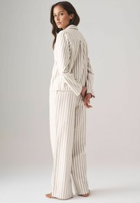 Pajama set s prugama u svijetlo bež i krem boji. Mekana tkanina, dugi rukavi, ovratnik i hlače opuštenog kroja.
