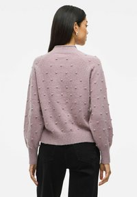 Liliowy sweter dzianinowy z fakturowanym wzorem kulek, prążkowanym dekoltem i mankietami oraz krótkim krojem, w zestawie z czarnymi spodniami.