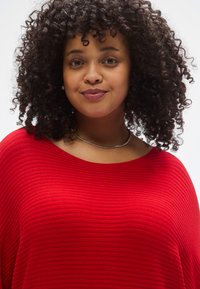 Κόκκινο τοπ με ραβδώσεις και φαρδύ ντεκολτέ, με άνετη εφαρμογή και ελαφριά υφή. Ένα επισημασμένο κολιέ προσθέτει λεπτομέρεια στο ντεκολτέ.