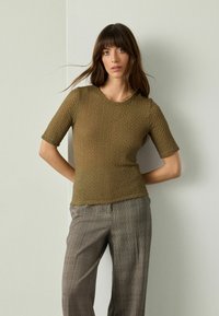 Olivgrünes T-Shirt mit Textur, kurzen Ärmeln und rundem Ausschnitt, kombiniert mit grauen Karohosen in lässiger Passform.