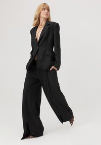 Czarna, strukturalna marynarka i spodnie o szerokich nogawkach z gładkiego materiału. Marynarka ma klapy i kieszenie; spodnie wyposażone są w boczne rozcięcia i akcenty w zwierzęcy wzór.