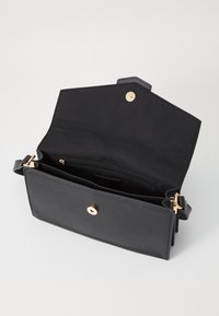 Bolso de mano de cuero negro con cierre de clip dorado y correa ajustable. El interior cuenta con un bolsillo con cremallera y compartimentos abiertos.