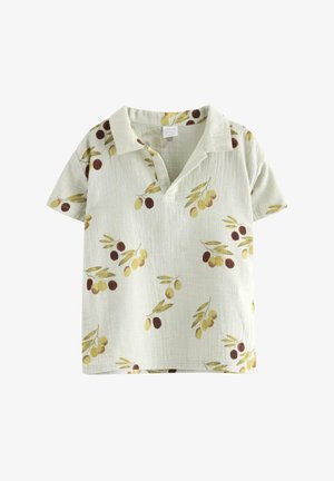 Chłopiec w beżowej koszuli w kwiaty z krótkim rękawem, brązowych szortach, beżowej czapce i zielonych sandałach stojący na białym tle.