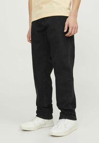 Svarta jeans i rak modell med synlig sömnad och en klassisk femficksdesign, kombinerat med vita löparskor.