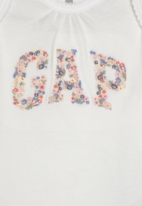 Camisola de alças em algodão branco com bordado floral em forma das letras "GAP" em várias cores, incluindo rosa, azul e verde.