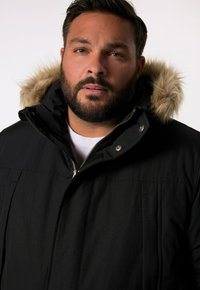 Svart zip-up parka med huva i fuskpäls, med strukturerad tyg, silverdetaljer och rak skärning.