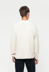 Lichtbeige gebreide trui met een geribbelde textuur, verlaagde schouders en een ronde halslijn, gecombineerd met donkere jeans.