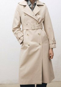 Trench-coat beige, croisé, ceinture à la taille, grands revers, détails de boutons, poignets avec lanières, texture lisse, longueur genou.