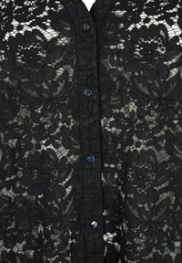 Svart blommig spetstyg med en vertikal rad av fem metallknappar ner i mitten.