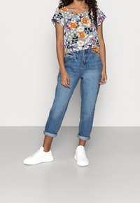 Kraťasová halenka s květinovým potiskem má na šedém pozadí vícebarevné květiny. Kombinována s světlými jeansy s ohrnutými manžetami a bílými teniskami.