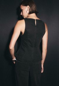 Czarny bezrękawnik z denimu o dopasowanym kroju, widocznymi szwami i ozdobnym wycięciem z tyłu. Połączony z czarnymi spodniami z denimu.