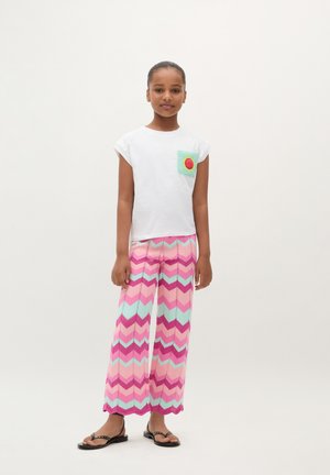 White short-sleeve t-shirt with a green and red crochet pocket, paired with pink and mint chevron-patterned wide-leg pants. Black sandals.
