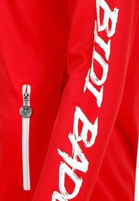 Tejido rojo con un cierre blanco vertical y una manga con texto blanco en negrita que dice "BADBOY" en una fuente desgastada.