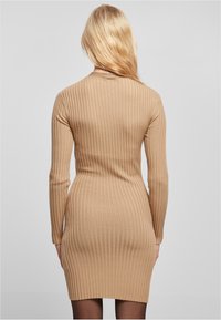 Robe bodycon à manches longues en beige, côtelée ; présente un tissu texturé et une silhouette ajustée, se terminant au-dessus des cuisses.