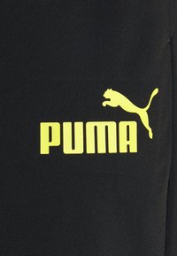 Logo Puma jaune avec un puma sautant et un texte en gras sur fond de tissu noir.