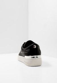 Černé tenisky s cvočkovými akcenty a kovovým podpatkem. Vyrobené z texturované kůže s gumovou podrážkou a logem na zadní straně.