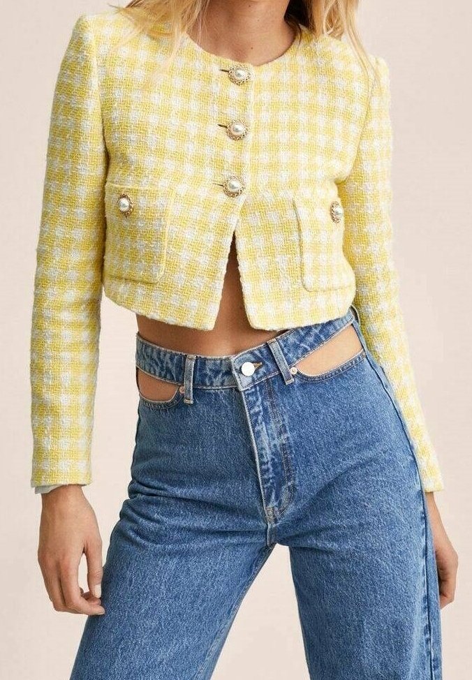 Femme portant une veste courte à carreaux jaune et blanc avec des boutons dorés et un jean bleu taille haute avec des découpes à la taille.