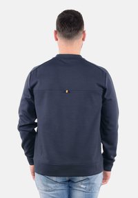 Felpa blu navy a girocollo in un tessuto liscio con orlo dritto e una piccola accentuazione arancione sul retro. Ideale per un look informale.