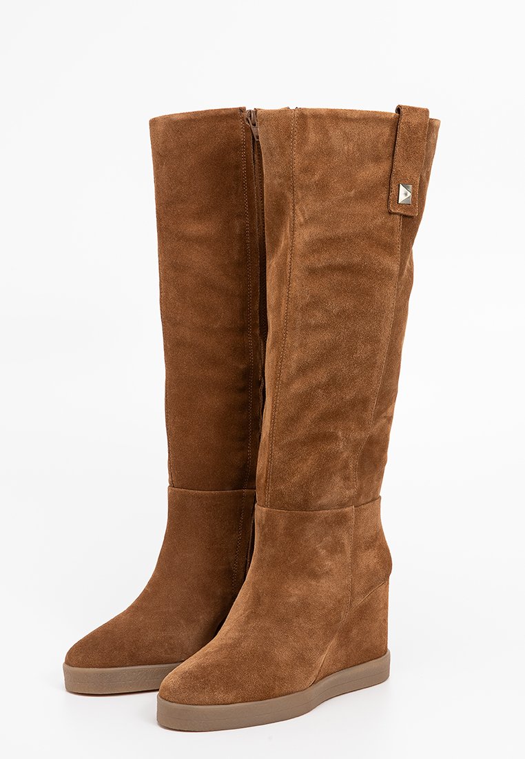 Bottes compensées en suède marron jusqu'aux genoux avec une fermeture éclair sur le côté, un bout arrondi et un petit accent métallique près du haut pour plus de détails.