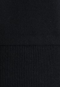 Lähikuva mustasta neulotusta kankaasta, jossa näkyy erilaisia neulekuvioita; yläosa on sileä ja alaosassa on resorineuletta.