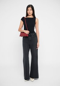 Čierny top bez rukávov, tmavošedé široké nohavice s vysokým pásom, biele baleríny s ostrou špičkou a malá červená crossbody taška. Jednoduché pozadie.