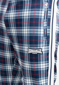 Marinegekleurde plaid joggers met rode en witte accenten, voorzien van een Lonsdale London logo patch en zijrits zakken. Soepele stoftextuur.