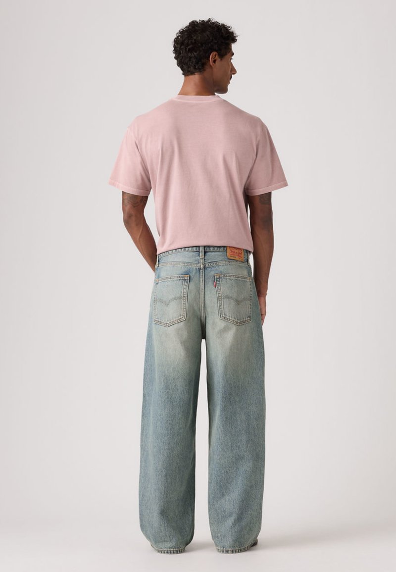 Kort lyserød bomulds t-shirt med op-rullede ærmer, kombineret med løstsiddende, lyseblå denimjeans med en falmet tekstur og tydeligt design på baglommen.