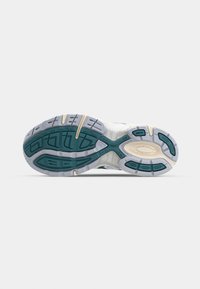 Semelle d'une chaussure de course montrant une bande de roulement en caoutchouc bleu-vert et gris avec des rainures courbes et un dessin ovale beige près du talon.
