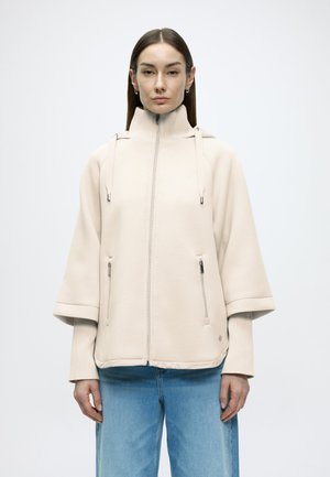 Beige zip-up jacket with a high collar, wide sleeves, and front zipper pockets. Made of soft fabric with smooth texture.