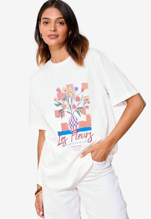 Valkoinen lyhythihainen T-paita, jossa on värikäs kukkavaasi grafiikka ja "Les Fleurs" -teksti alareunassa. Pehmeä puuvillasekoitekangas.