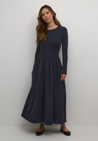Navy blue long-sleeve dress with a ribbed bodice and a flowing pleated skirt. Smooth fabric with a round neckline and fitted sleeves.