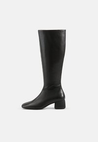 Bottes noires en cuir montant jusqu'au genou, avec un bout carré et un talon épais, présentant une texture lisse et un design minimaliste.