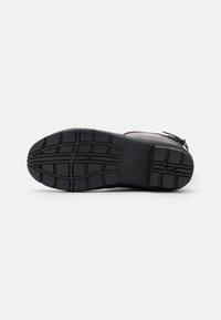 Semelle de botte en caoutchouc noir présentant un motif de relief texturé, avec de profondes rainures pour une adhérence et une surface uniforme pour la stabilité.