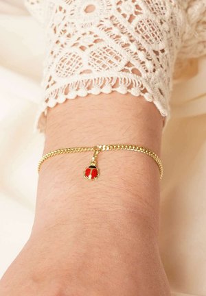 Gold chain bracelet with a small red and black ladybug charm worn on a wrist with a white lace sleeve visible.