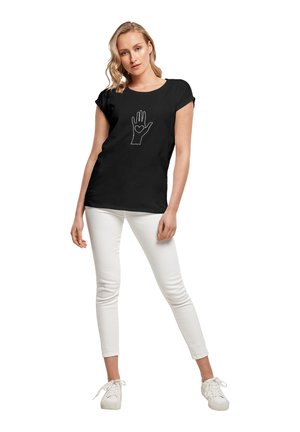 Sort kortærmet t-shirt med en hvid stregtegning af en hånd med et hjerte i håndfladen, parret med hvide tætsiddende bukser og sneakers.