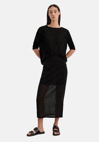 Schwarzes, lockeres Stricktop mit langen Ärmeln, kombiniert mit einem schwarzen, semi-transparenten Maxirock und flachen schwarzen Sandalen. Einfaches Design und Textur.