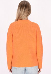 Orangen gerippter Pullover mit langen Ärmeln, Rundhalsausschnitt und lockerer Passform. Hergestellt aus strukturiertem Material, endet auf Hüfthöhe.